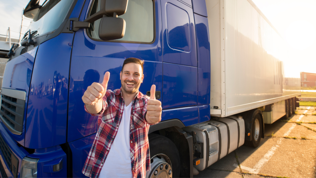 駐車しているトラックを背景に男性が両手で「グッド」ポーズを笑顔でしている画像