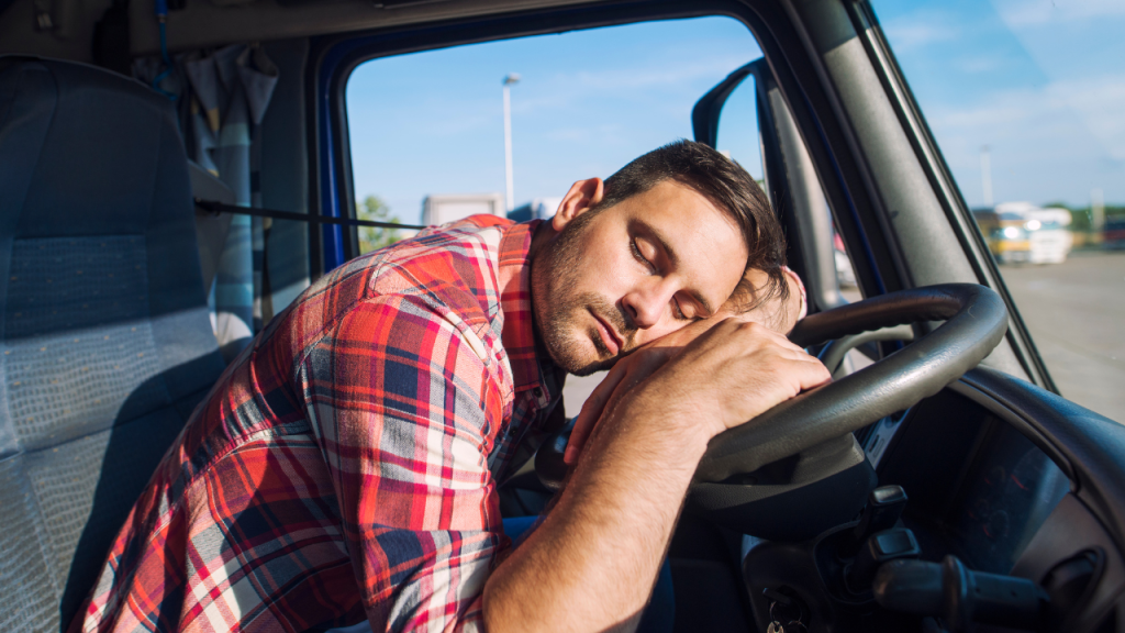 トラックドライバーが運転席でハンドルを枕にして眠っている画像